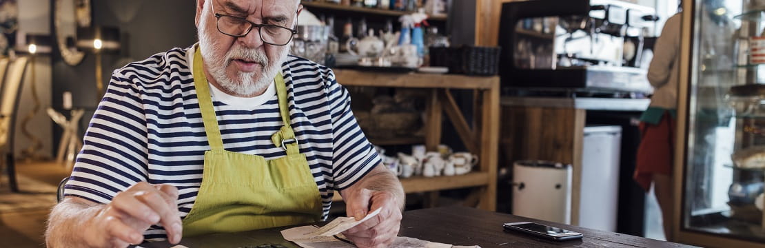 Man sits at a table in a workshop with receipts and a calculator.